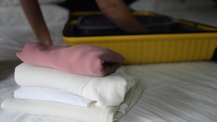 Fototapeta premium Woman carefully packing clothes into yellow suitcase on hotel bed