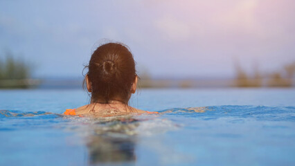 Woman relaxing in infinity pool enjoying ocean view