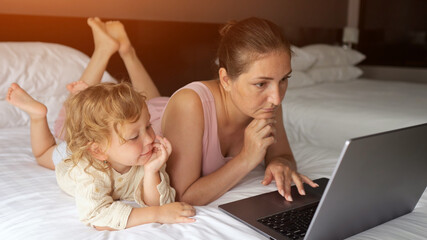 Woman working on laptop with child on bed in hotel room