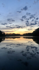 Beautiful sunset reflecting on a calm lake surrounded by trees and a dramatic sky