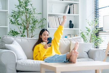 Happy young asian woman relax on comfortable couch at home texting messaging on smartphone, smiling girl use cellphone, chatting online message, shopping online from home