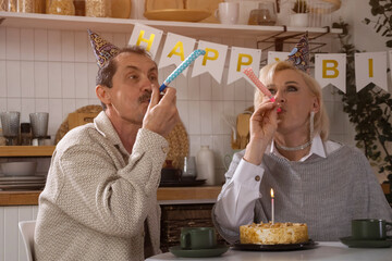 Senior couple blowing party blowers celebrating birthday at home