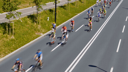 Group of cyclists pedal down a wide, empty road, creating a sense of freedom and adventure. Aerial view highlights their journey and camaraderie.
