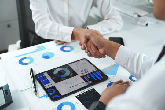Business people shaking hands over financial charts and digital tablet