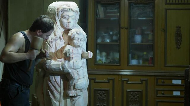 Woodcarver artisan carefully crafting Madonna sculpture with traditional chisel and mallet, revealing intricate artistic details inside rustic workshop, slow motion