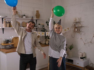 Senior couple wearing party hats and holding balloons celebrating birthday