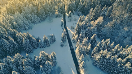An aerial view of a winding road through a snowy forest, with a car driving along the route,...