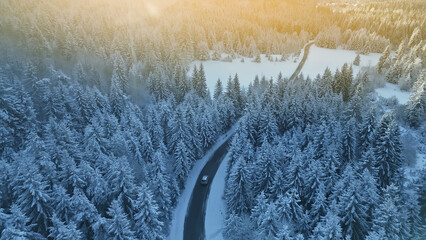 Aerial view of a winding road through a snowy forest, with a car driving along the path. Scene evokes a sense of adventure and alpine travel, showcasing the beauty and challenges of winter driving.