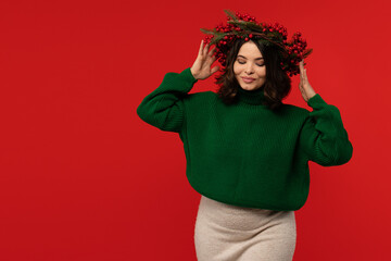 Woman in green sweater wearing a festive wreath of red berries and pine branches