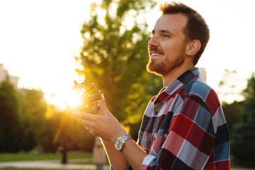Smiling young man holding globe illuminated by golden sunset. Astronomer holds an armillary sphere outside during an open class on spherical astronomy