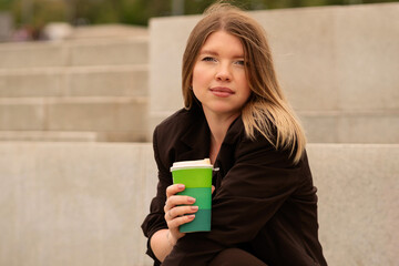 Young woman sitting on steps wearing brown suit and white sneakers. Natural feel with soft light. Casual, confident pose and expression add genuine and approachable vibe.