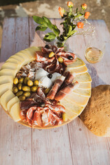 Catering on a wooden board on a rustic table, meat, olives, cheese, and a drink as an appetizer