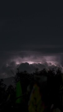 Vertical video. Multiple Lightning Strikes Illuminate Towering Thunderclouds Above Mountain Range at Night on a Tropical Island in Continuous Time-Lapse Sequence