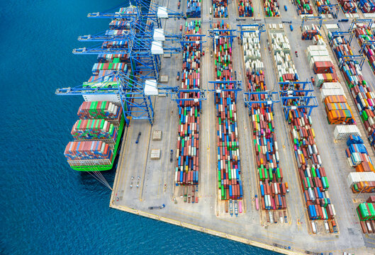 Aerial view of a large container terminal port with loading activity of a cargo vessel by cranes and trucks