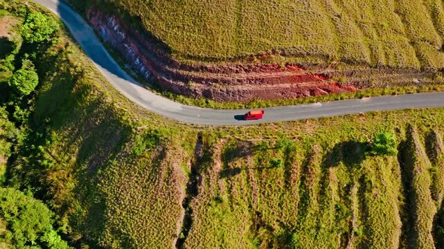 Aerial view of a red Taxi Brousse navigating a winding mountain road through the dramatic and colorful terrain of Madagascar. Perfect for transport, travel, and landscape themes.