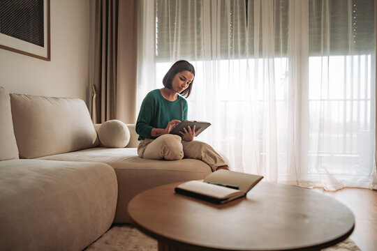 A woman on a sofa using a tablet, illuminated by beautiful natural light