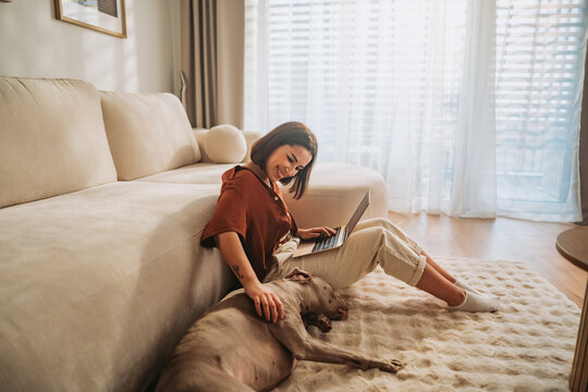 A woman works on her laptop at home, enjoying a cozy moment with her dog - Powered by Adobe