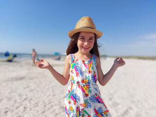 Portrait of adorable young girl on the beach in summer dress and hat
