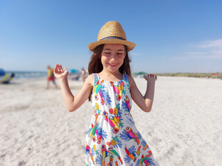 Portrait of adorable young girl on the beach in summer dress and hat