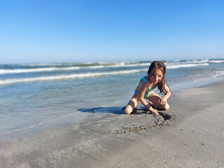 Smiling kid, girl playing in the sand at beach, sea waves in the background