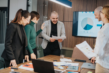 A group of coworkers engaging in a productive business meeting, sharing ideas and reviewing data on charts in a modern office setting, fostering teamwork and collaboration.