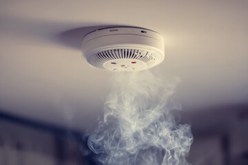 Smoke detector on ceiling emits smoke in soft lit room, highlighting its safety function