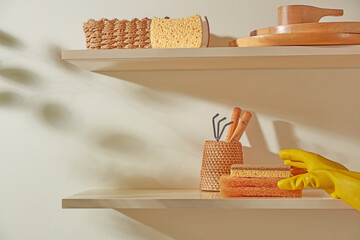 Shelf with a stack of orange towels, brushes, and gloves. A clean and artistic composition reflecting soft, warm tones of everyday kitchen life.