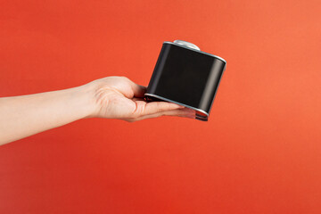 Black can for packaging in hand on red background.