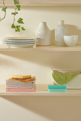 White dishes, pink sponges, and small plants displayed on a clean kitchen shelf with soft light coming through the window. Bright and peaceful home vibes.
