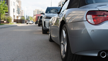 Line of parked cars along a city street in a residential area, captured from a low rear-side angle...
