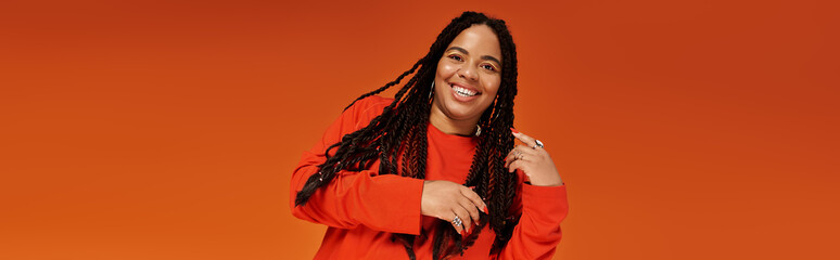 Stylish woman with braids enjoying a vibrant moment against an orange backdrop