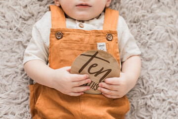 a baby boy holding a ten months old milestone round wooden sign 