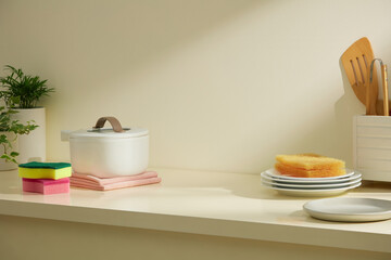 White dishes, a cleaning tool, and a sponge placed beside food items on a shelf. Soft shadows make this a bright yet practical kitchen view.