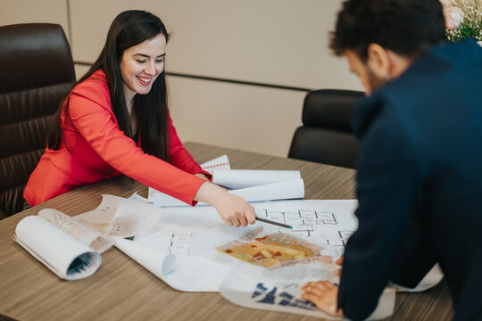 Two business people collaborating on architectural plans in a modern office environment. The image reflects teamwork, professional collaboration, and strategic planning in a corporate setting.