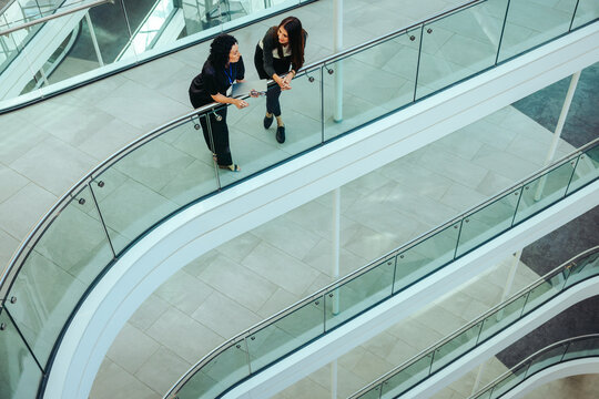 Fototapeta Two female coworkers conversing on a modern office flyover