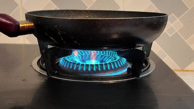 Close up of a blue flame on a gas stove burner in a dark kitchen, highlighting the energy and heat used for cooking