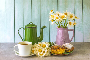 Summer breakfast still life; cup of coffee, hot croissants, bouquet of white daisies and vintage coffee pot on a table