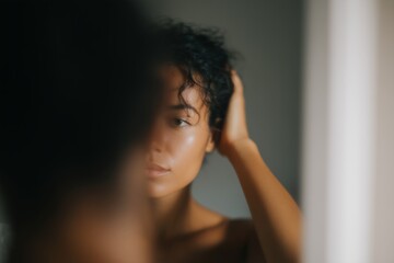 Fototapeta premium Quiet Morning Routine: Person in Soft Daylight Putting on Earrings at Mirror