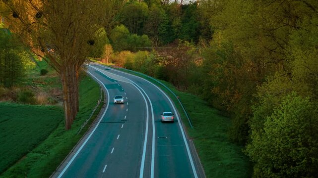 Passenger car moving along winding paved road between trees. Sedan driving on curvy asphalt route surrounded by forest. Vehicle traveling through serpentine tarmac path bordered by woods