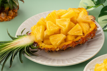 Fresh pineapple chunks served in a pineapple bowl on green table background.