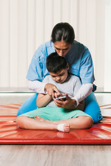 Physiotherapist helping child with cerebral palsy using smartphone during rehabilitation session