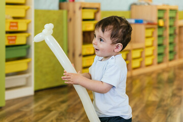 Happy toddler boy playing with giraffe balloon in kindergarten
