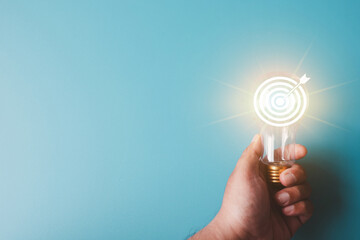 Hand holding a lightbulb with a glowing target board and arrow icon inside. Concept for business strategy, setting clear objectives, marketing goals, innovative solutions,creative mindset.