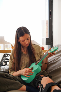 Teen girl with cast on leg playing ukulele at home