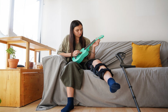 Teen girl with leg injury playing ukulele on sofa