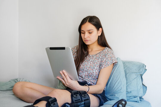 Teen girl with broken leg using tablet on her bed at home
