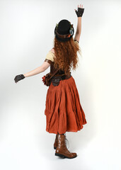 Full length walking portrait Steampunk Botanist, mad scientist, female model in Victorian Costume with top hat and goggles. Redhead Fantasy Character Posing on White Studio Background

