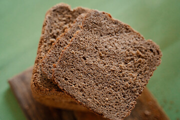 Texture of homemade black dark Darnitsky rye bread on a wooden board on a green napkin close-up