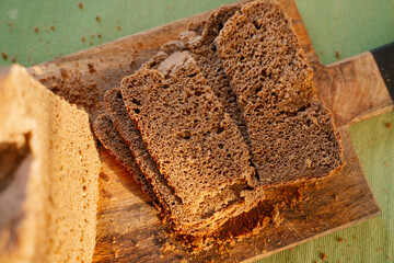Homemade black dark Darnitsky rye bread with sun light on a wooden board on a green napkin close-up. A lots of fresh bread crumbs on the board, it looks very appetizing, invites to a healthy snack.
