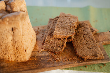 Homemade black dark Darnitsky rye bread with sun light on a wooden board on a green napkin close-up. A lots of fresh bread crumbs on the board, it looks very appetizing, invites to a healthy snack.